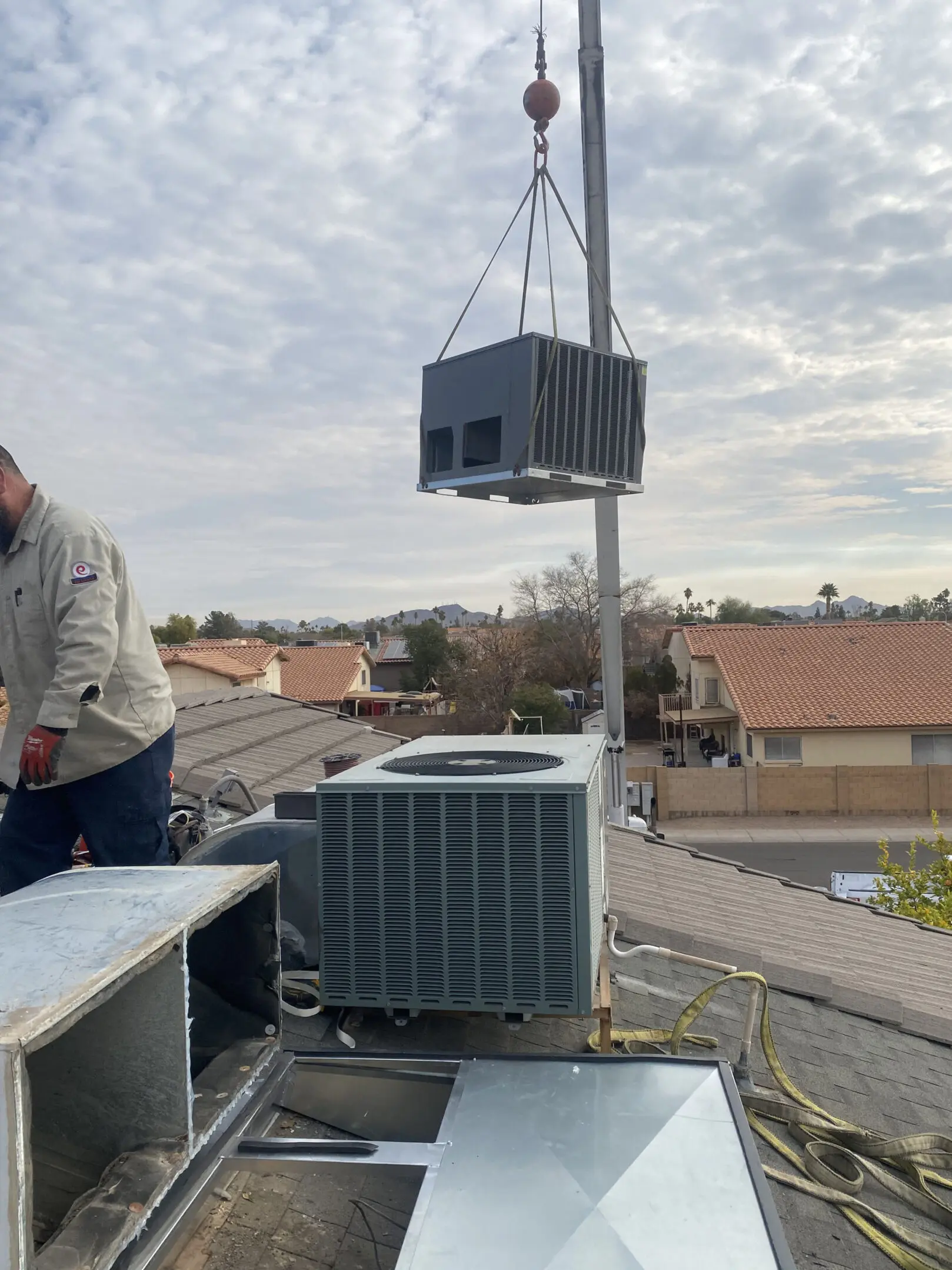 A man standing on top of a roof next to an air conditioner.