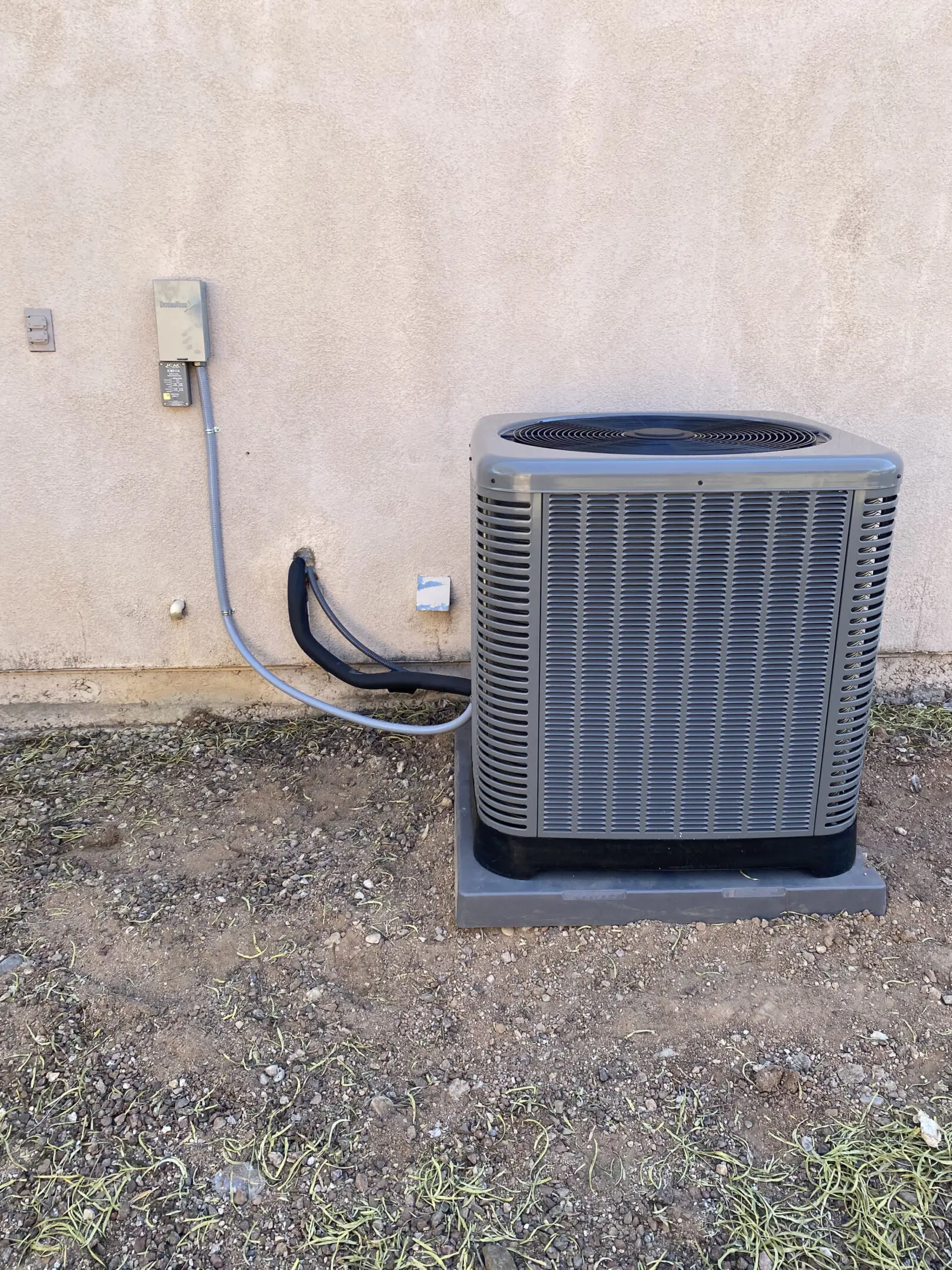 A gray air conditioner sitting outside of the wall.