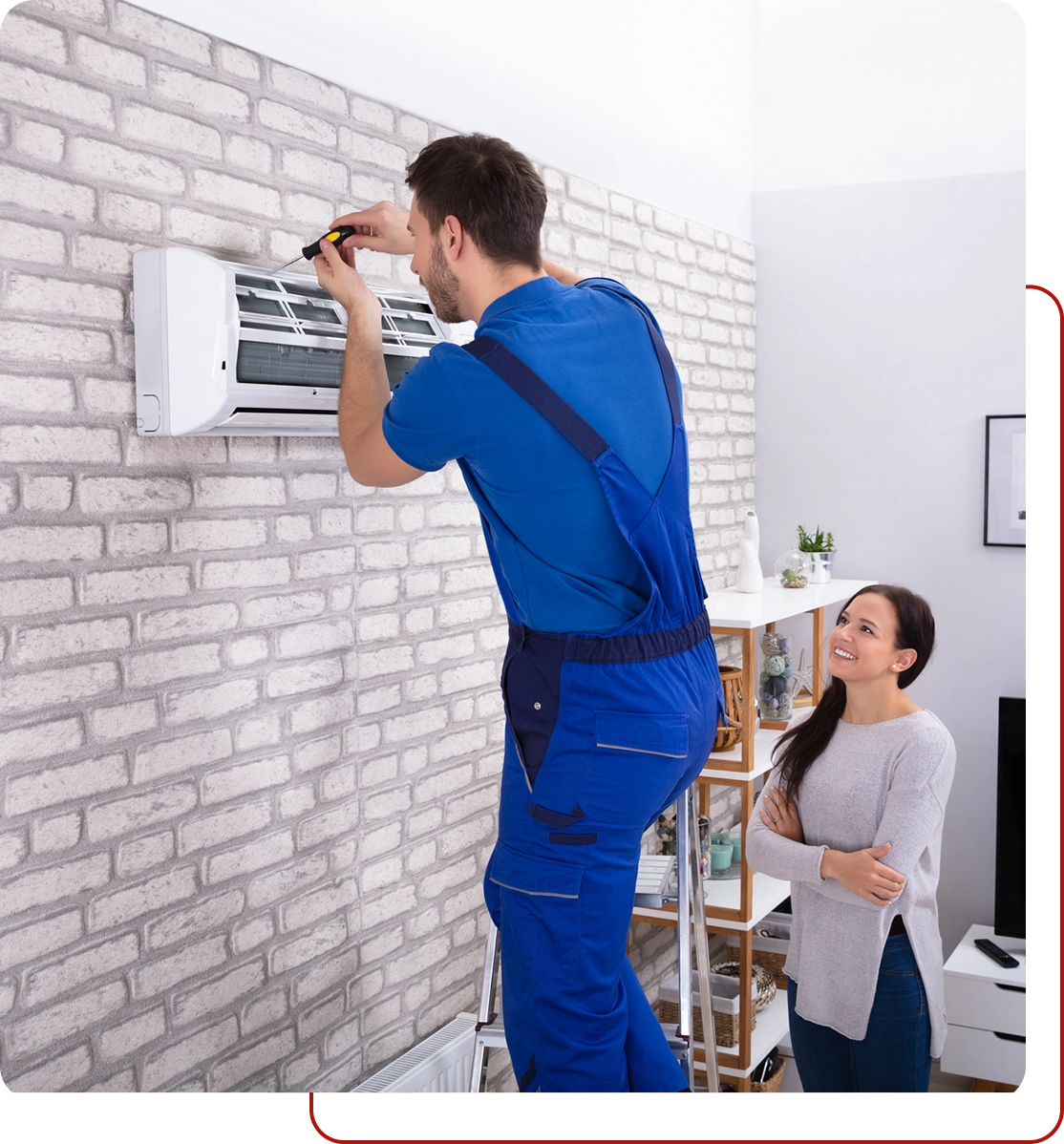 A technician in blue overalls skillfully repairs a wall-mounted air conditioner, showcasing the quality of affordable HVAC services, while a woman watches and smiles.