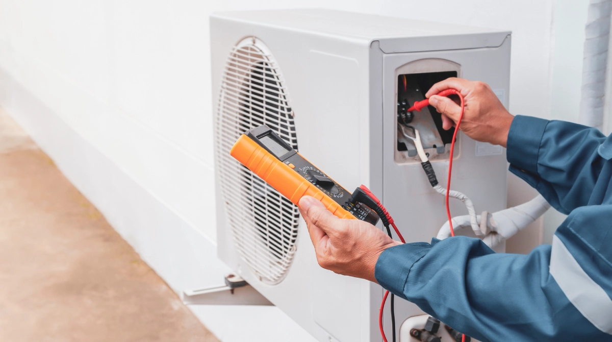 A technician from HVAC Installation Services uses a multimeter to measure voltage on the outdoor unit of an air conditioning system.