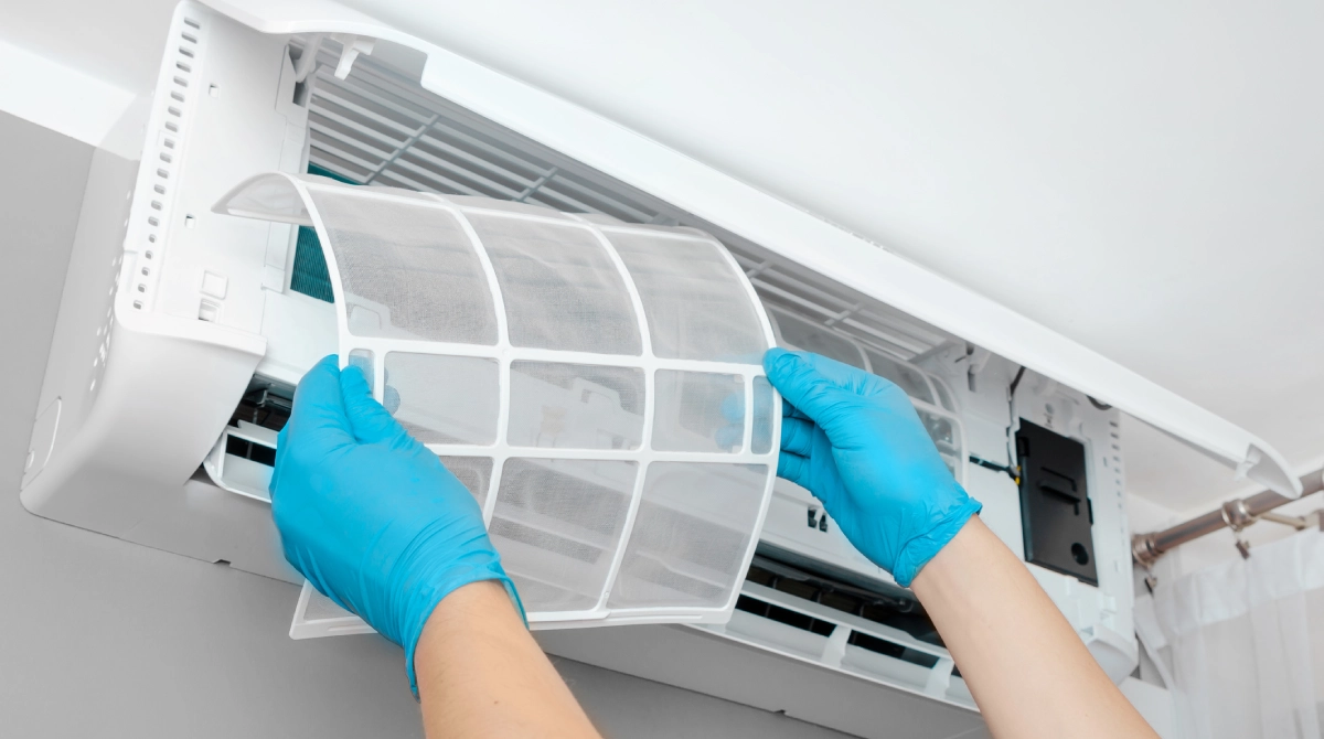 Hands in blue gloves expertly replacing or cleaning a filter in a wall-mounted air conditioning unit, showcasing the precision involved in HVAC installation services.